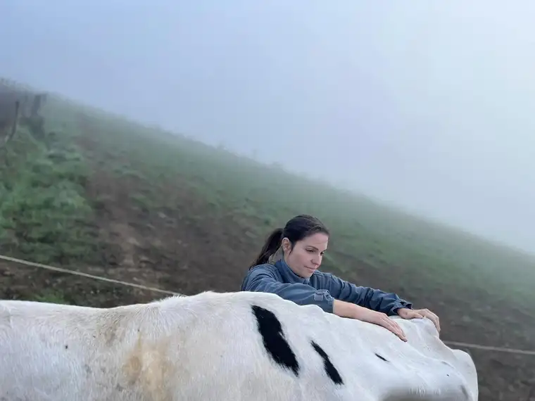 Marine Boullier, une main posée sur le dos d’une vache, dans un pré au petit matin