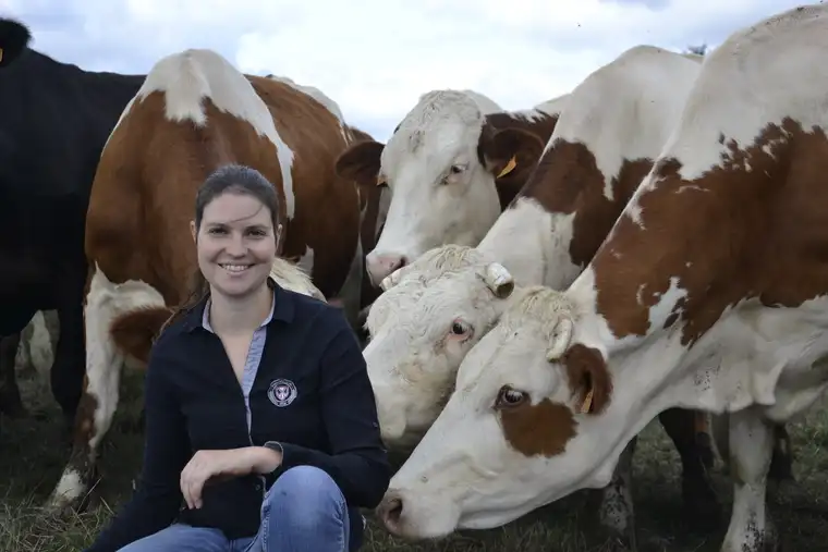 Marine Boullier souriante, accroupie devant trois vaches dans un pré